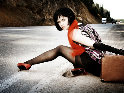 девушка, позирует, сидя на дороге, с чемоданом